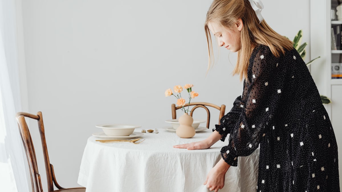 A woman with long blonde hair arranging a table with flowers and elegant dishware.