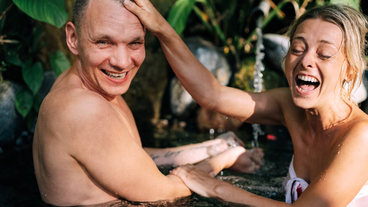 Happy couple laughing and playing in a natural water setting, enjoying a relaxed time together.